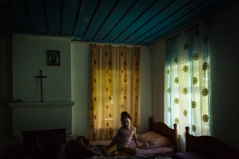Girl sitting in bed in blue room with gold and aqua curtains and a cross on the wall