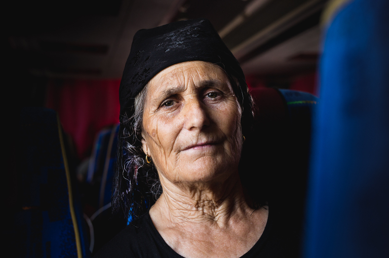 Widowed elderly Albanian woman sitting on a bus wearing a black headscarf and dress in dramatic natural light