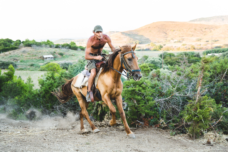 Middle aged fit looking shirtless man riding brown horse at a gallop in Skyros Greece