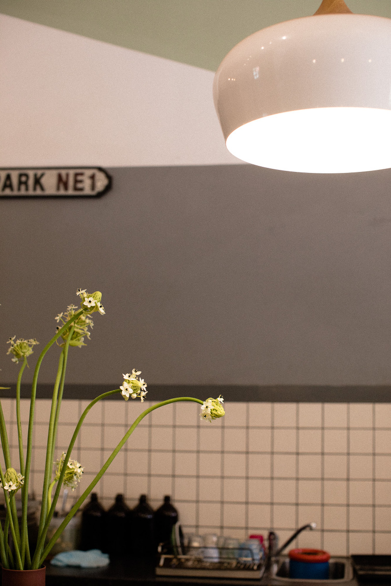 cafe bench with low hanging white lamp and small flowers in jar against grey wall