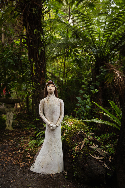 Sculpture of whimsical cloaked woman by Jenny Rowe standing in green ferny forest