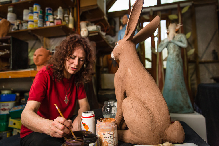 Sculptor Jenny Rowe with curly dark hair preparing her tool to work on a large hare sculpture