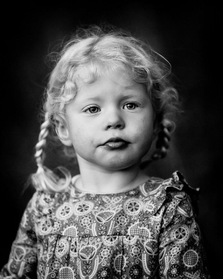 Toddler girl with blonde hair in plaits staring into distance with lips slightly puckered