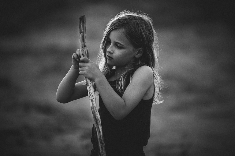 Strong looking girl standing in backlight at beach scratching at a tall stick