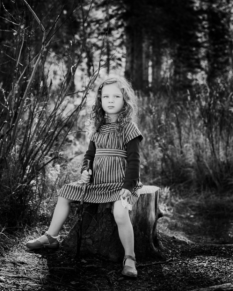 Strong looking girl sitting on stump with straight back and holding stick looking into distance