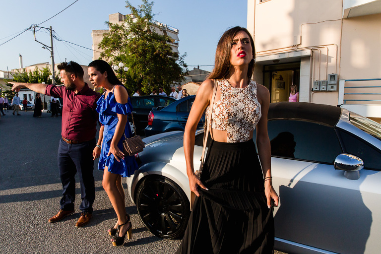 Three Greek wedding guests waiting in carpark with slightly unflattering expressions