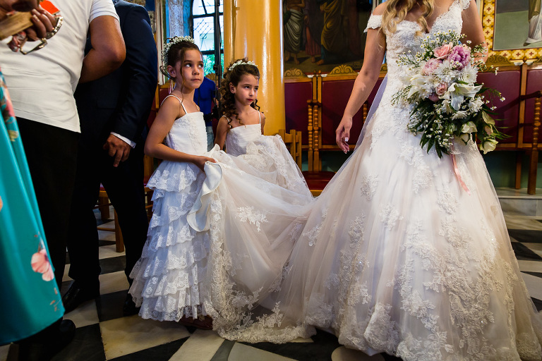 Two flower girls holding bride's dress train looking uncertain