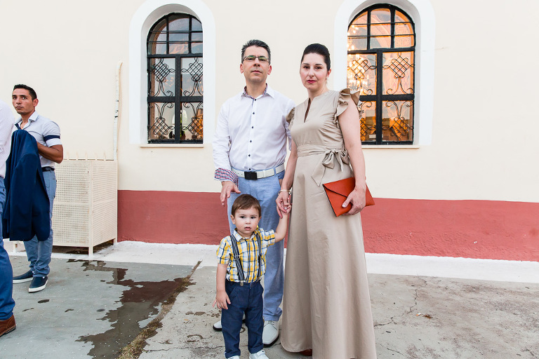 Sombre looking family stand in front Greek Orthodox church dressed formally looking at camera