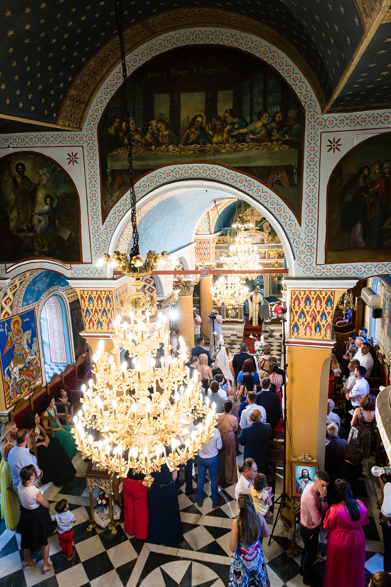 Ornate chandelier and decorations on ceiling in packed Greek church for wedding