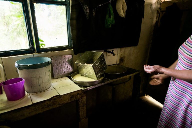 lady's wet hands beside sink where she is making cheese in small dark room