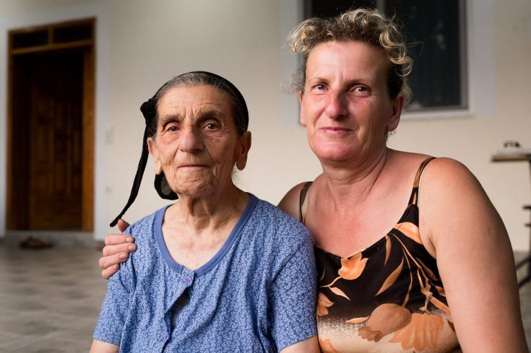 Elderly Albanian lady wearing black scarf being embraced by her adult daughter