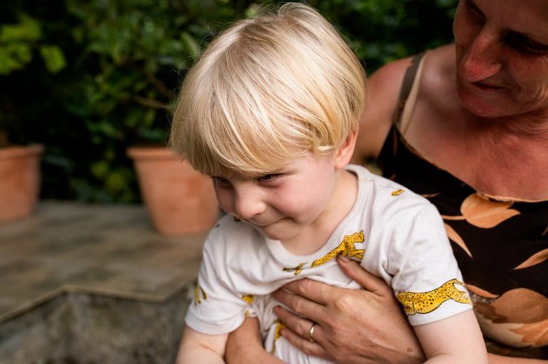 Older lady embracing young blonde haired boy who looks shy and happy