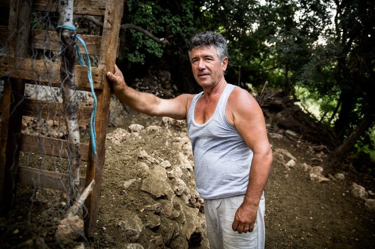 Albanian man looking at camera wearing singlet with sweat marks leaning on improvised gate made of wood pallet
