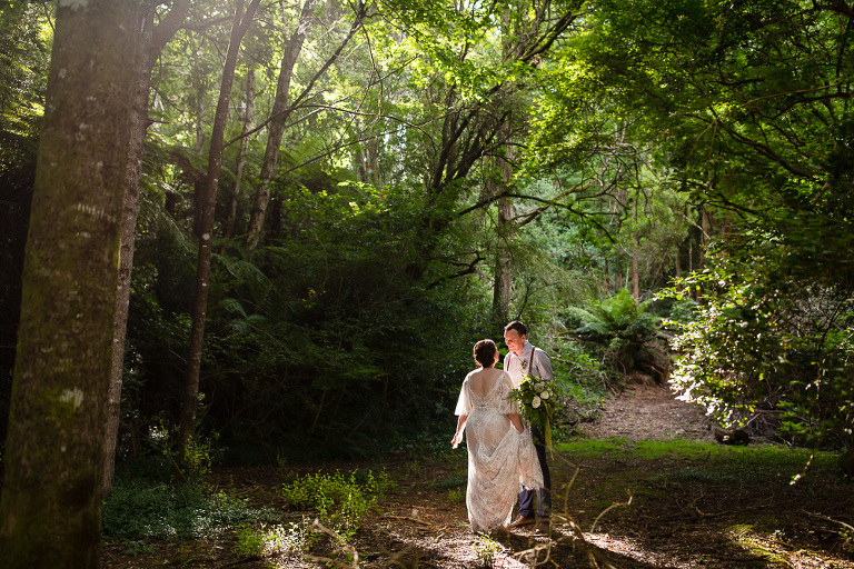 bride and groom in patch of light in forest looking at each other