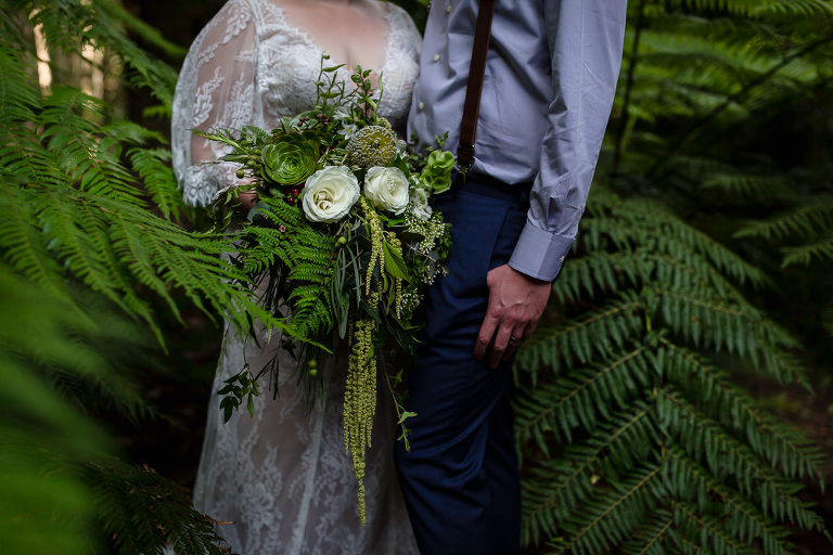 bride and groom standing with bridal bouquet among ferns
