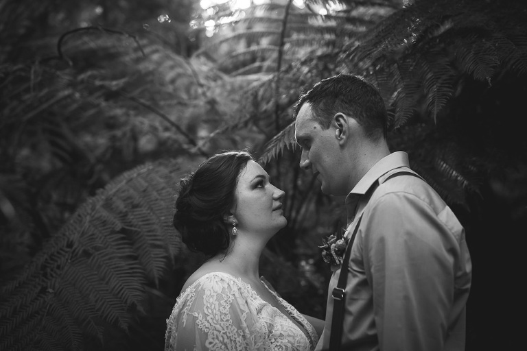 bride and groom looking at each other intently with ferns behind them