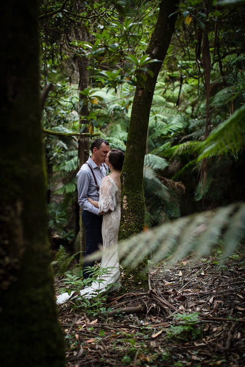 bride and groom kissing against a tree in ferny forest