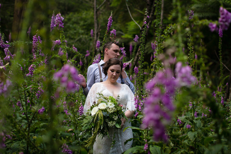 bride and groom standing among many purple fox glove flowers outdoors