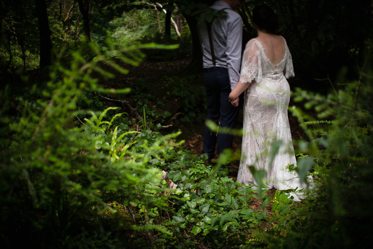 bride and groom walking away from green ferns outdoors into shadows
