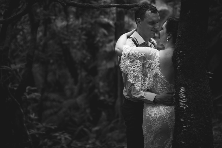 bride and groom embracing leaning against tree looking at each other in ferny forest in black and white